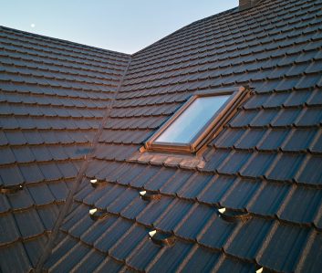 Closeup of attic window on house roof top covered with ceramic shingles. Tiled covering of building Closeup of attic window on house roof top covered with ceramic shingles. Tiled covering of building.