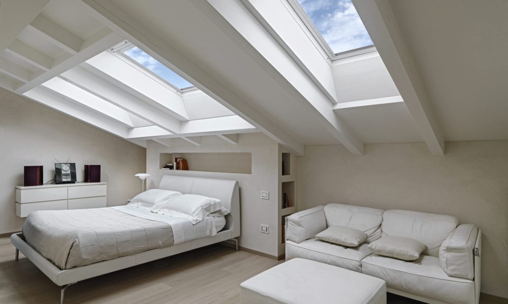 interior shot of a modern bedroom in the attic interior shot of a bedroom in the modern attic-room in the foreground the leather sofas with footrest in the background there is the bed illuminated by two skylights